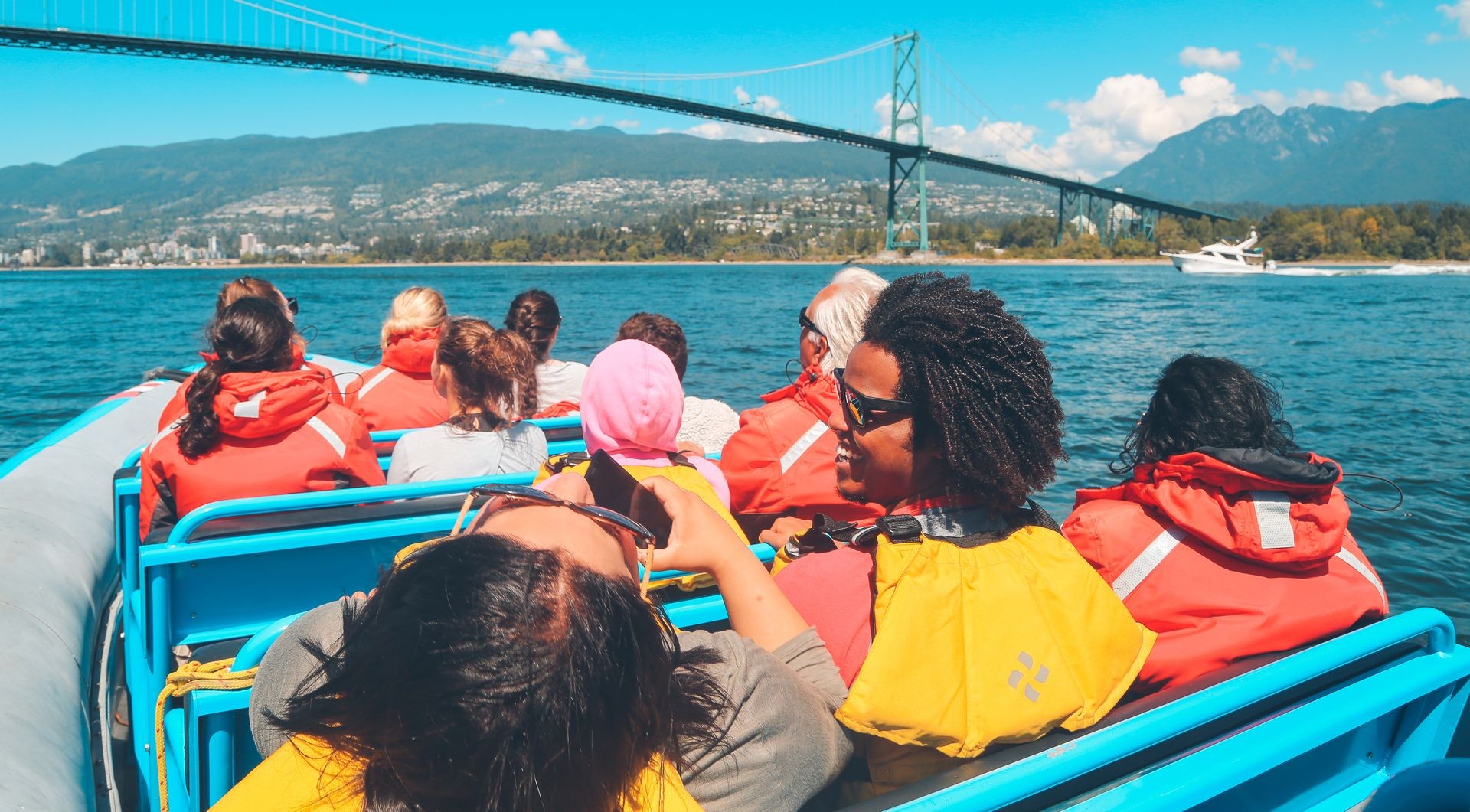 Tourists in red jackets on a boat with a distant view of a bridge and mountains.