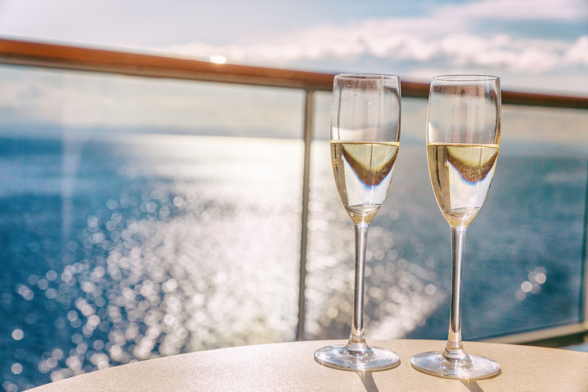 Luxury cruise ship travel champagne glasses on balcony deck with ocean sunset view on Caribbean vacation. Drinks in sun flare on cruise holiday destination.